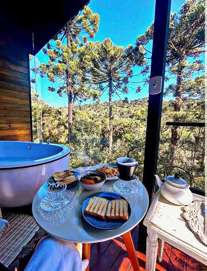 Café da manhã no deck ao lado da banheira, com araucárias e céu azul ao fundo